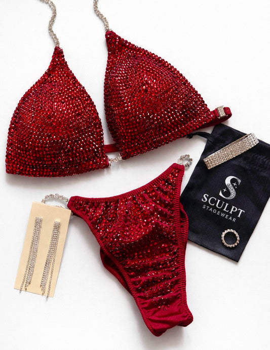 Red bikini set with rhinestone details on a white background, featuring a 'Sculpt' branded pouch.